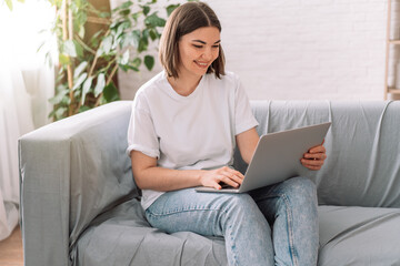 Naklejka premium Lady sitting on gray sofa reading with laptop.