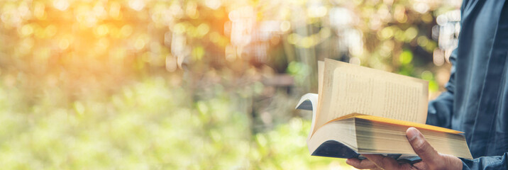 Banner Asian man holding book reading magazine at green park in natural garden. Relax man read open book. Panorama men happy learning. Closeup Men hands open textbook in green park with copy space