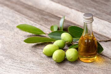 Olive oil in glass bottle and green olive fruit with leaves on wooden table background. 