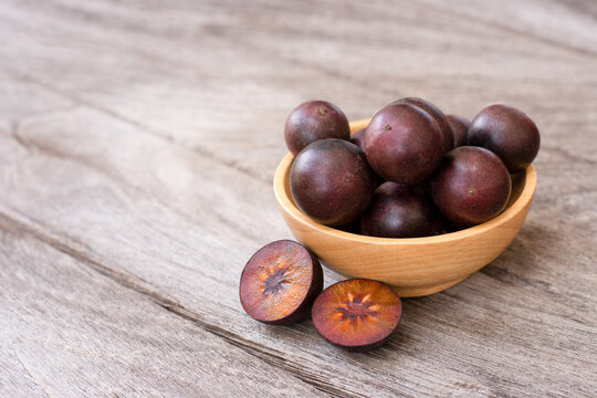 Flacourtia indica fruit with half sliced isolated on wooden table background.