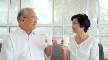 Happy Asian elderly couple relaxing and drinking milk on the sofa at home. Happy senior retirement lifestyle