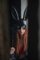 Beautiful girl a dancer in the rabbit mask smokes a cigarette on the dark background.