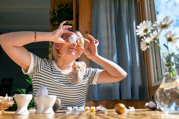 Smiling woman preparing easter decoration at home, painting colorful easter eggs and coloring egg cups.