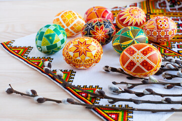 colorful traditional Ukrainian Easter eggs and willow twigs on the background of an embroidered towel and a wooden table - obrazy, fototapety, plakaty