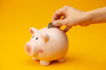 Close up, hand putting coins into the piggy bank.
Man making savings. Financial planning concept.