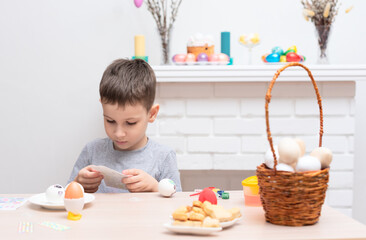Child boy decorating and painting easter eggs against defocused fireplace with Easter decorations...