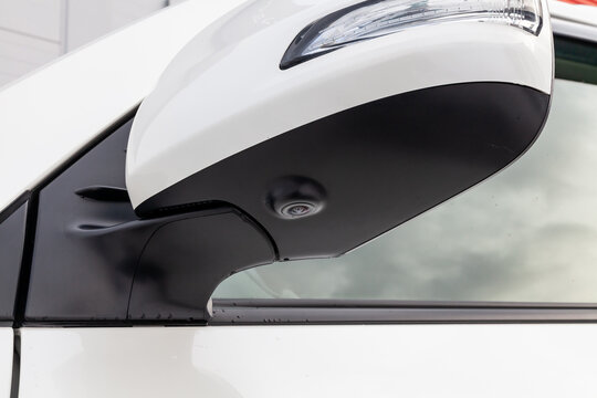 Close-up of the side left mirror with rear veiw 3d camera and window of the car body white SUV on the parking after washing in auto service industry. Road safety while driving