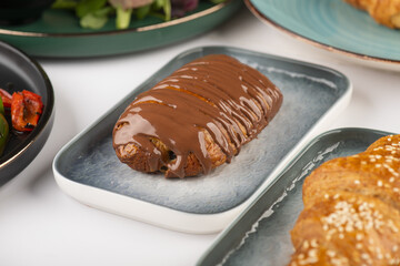 Fresh croissant with chocolate filling and chocolate topping in a plate on white background  