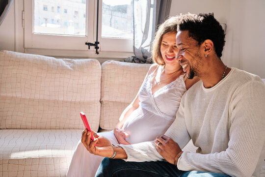 Multiethnic pregnant couple having a video call with a mobile phone at home.