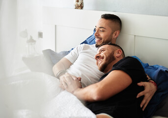Male gay couple smiling while relaxing in bed together.