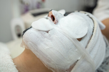Fototapeta na wymiar Closeup of cosmetologist applying white cosmetic facial mask for her female patient at spa salon