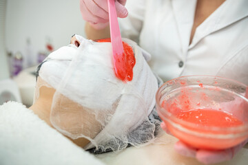 female medical worker applying on face red alginate mask her client  in beauty salon