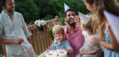 Multi generation family celebrating birthday and have garden party outside in the backyard on patio.