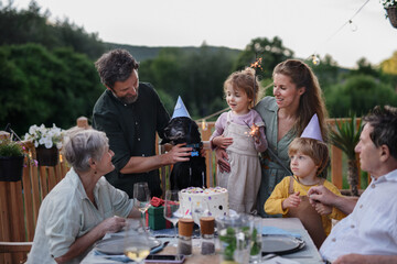 Multi generation family celebrating birthday of their dog and having garden party outside on patio.