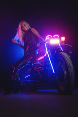 Naklejka na ściany i meble Young beautiful girl in the neon lights stands near the motorbike.