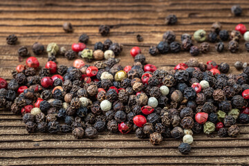 Peppercorns on dark rustic wooden background. Mix of different peppers