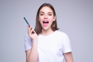 Obraz premium Young woman using phone device gadget app isolated over studio background. Girl holding a smartphone, chatting by mobile phone. Girl using phone, studio portrait. Woman makes telephone call on phone.