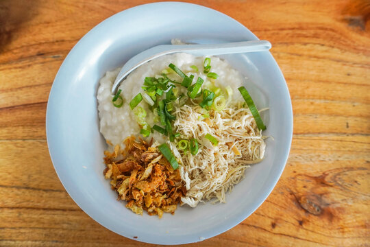 Indonesian Chicken Porridge, Indonesian Traditional Food Consist of porridge mixed with chicken meat served with egg, vegetables, and crackers on blue plate isolated on white background