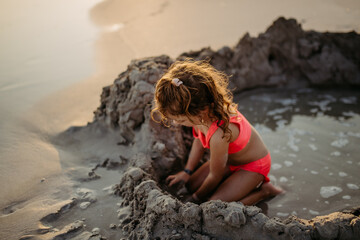 Little girl playing on the beach, digging hole in sand.