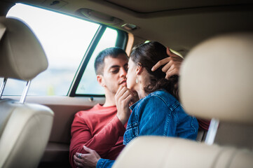 Passionate kiss in car. Young sexy couple in love, sitting in the back seat, looking and kissing...