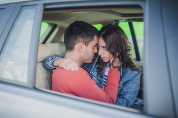 Passionate kiss in car. View through the window. Young sexy couple in love, sitting in the back seat, looking and kissing passionately each other, just before sex. Desire, passion and love concept