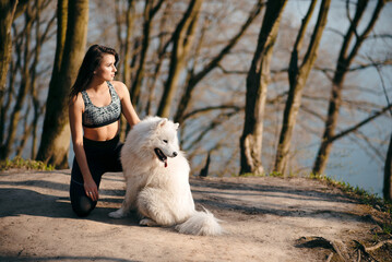 Beautiful sporty girl in hugging white purebred dog outdoors
