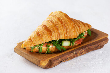 French croissant sandwiches with salmon, cream cheese and arugula on wooden board.