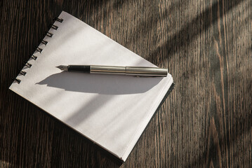 Otwarty notes z pustymi kartkami, na których leży otwarte pióro. Notes na stole w promieniach słońca.