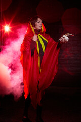 Witch woman in red cloak with skull on black background and light in night. Female warrior in the Dark