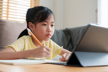 Asian little girl doing homework, learning, student using digital tablet at home - 578248328