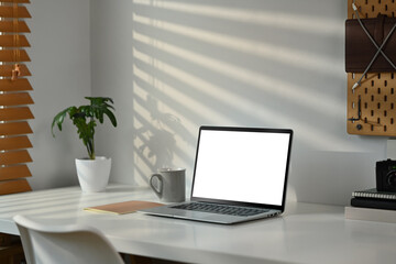 Fototapeta premium Laptop computer, coffee cup, books and potted plant on white table. Blank screen for text information or content