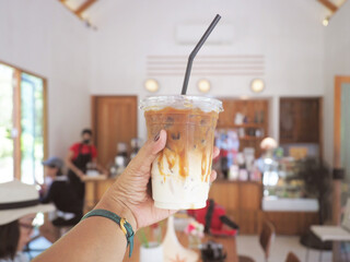 hand holding glass of iced coffee in coffee shop.