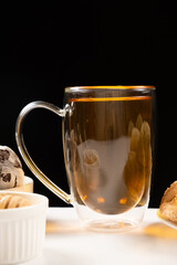 A cup of strong black tea, a glass large cup with a double bottom on a black background.