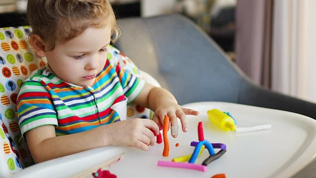 Little girl plays with multi-colored plasticine, creates different shapes