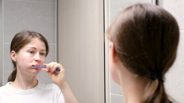 Young woman brushing teeth standing in front of mirror, oral care concept.