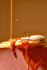 The eclair is poured with orange glaze and sprinkled with pistachios on an orange background....