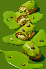 Art with an eclair. Broken eclair in puddles of icing on green background. Conceptual monochrome food poster for pistachio profiteroles