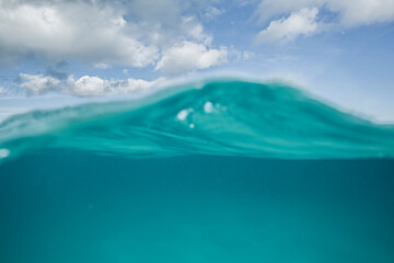 A split level shot of turquoise ocean water and clouds in a blue sky