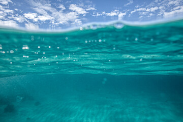 A split level shot of turquoise ocean water and clouds in a blue sky