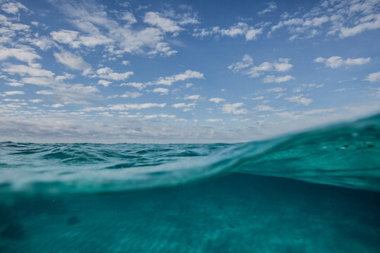 A split level shot of turquoise ocean water and clouds in a blue sky