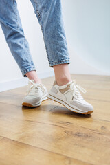 Close-up of female legs in jeans and casual sneakers. Women's comfortable casual shoes. White leather women's sneakers