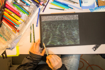 The hands of an older woman work on a drawing in her art studio.
