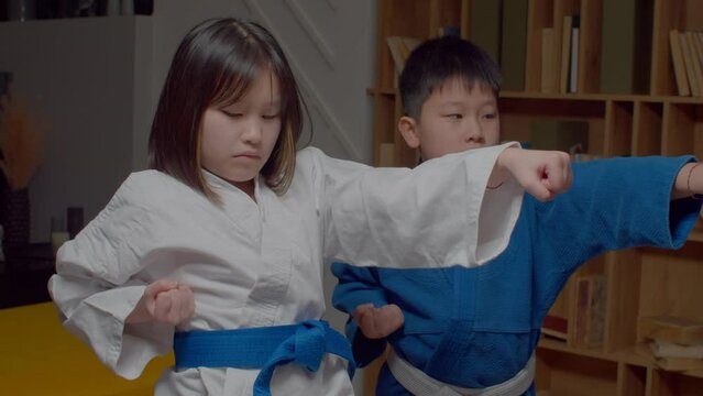 Portrait of concentrated motivated cute Asian preadolescent taekwondo students in uniform practicing martial arts with trainer, improving middle punch techniques during indoor workout.
