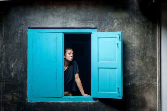 Caucasian girl in black t-shirt watching out a blue wooden window