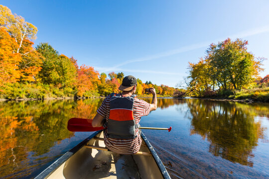 A man snaps a cell phone photo from a canoe in a Maine river. Fall.