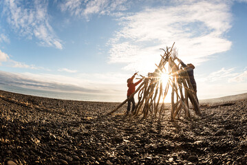 Two kids working together to build with driftwood at a beach