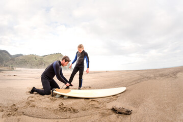 Adult man helps girl fasten surfboard leash at a beach