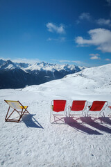 Deck chairs stand in the snow on the top of the mountain