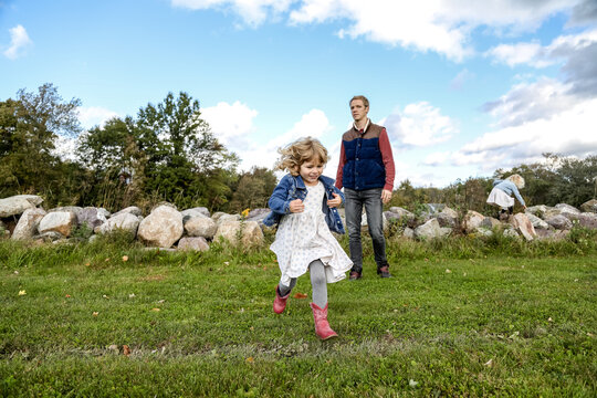 Little Girl Running Toward Camera Away From Dad In Field