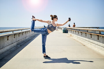 Full length of woman practicing standing half bow pose on pier during summer